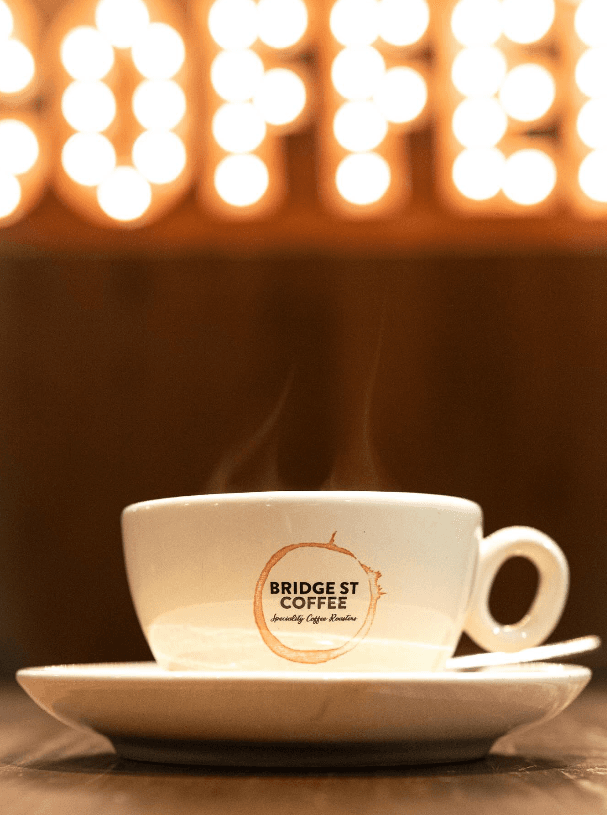 Latte under glowing coffee sign at Bridge St Coffee